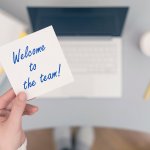 Femme assise tenant une note avec une phrase souhaitant la bienvenue à l'équipe