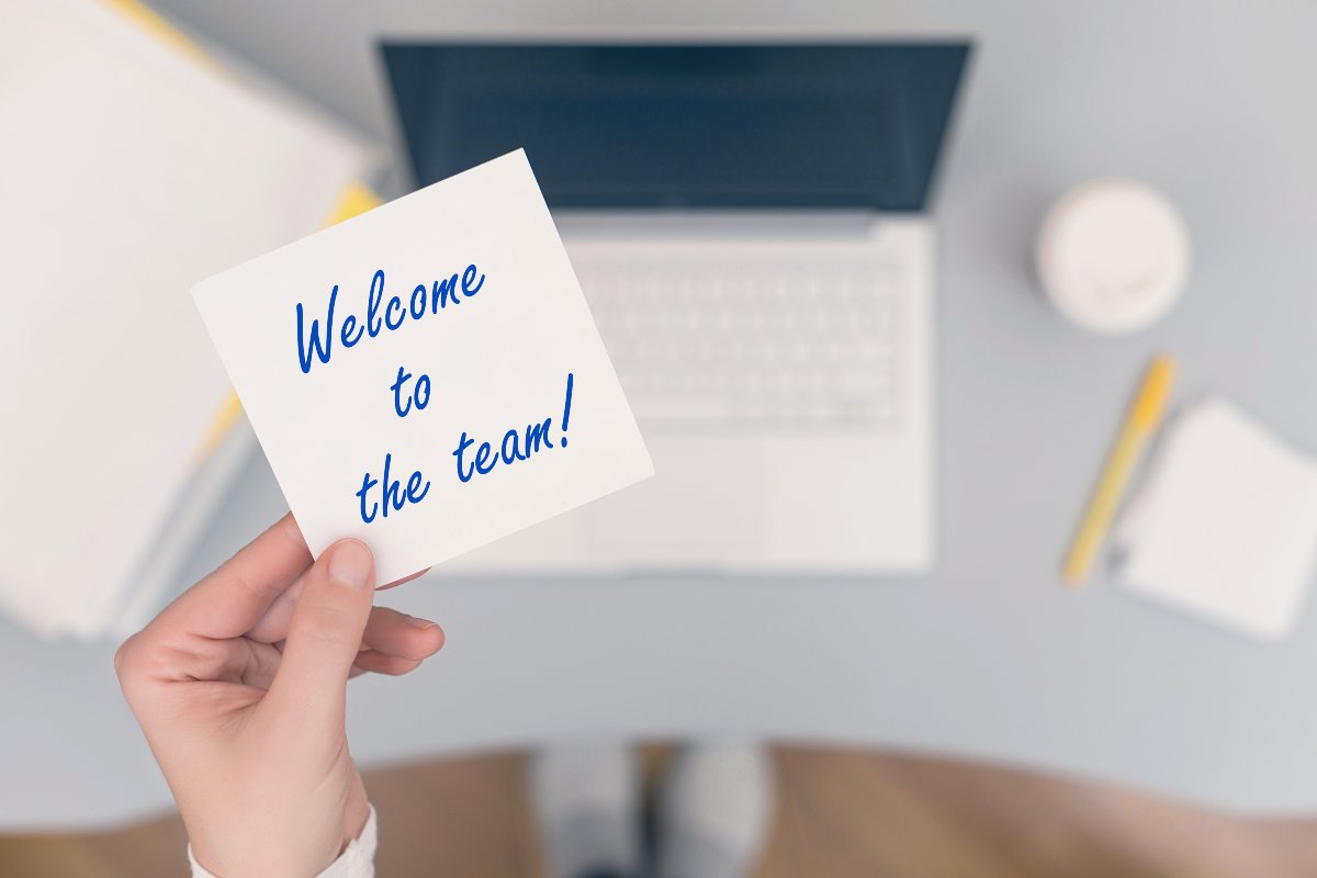 Femme assise tenant une note avec une phrase souhaitant la bienvenue à l'équipe